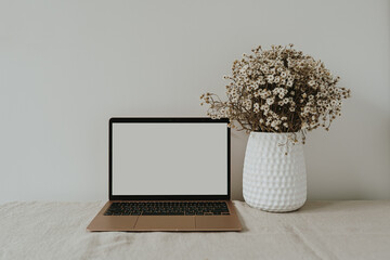 Laptop computer with blank screen on table with chamomile flowers bouquet. Aesthetic influencer...