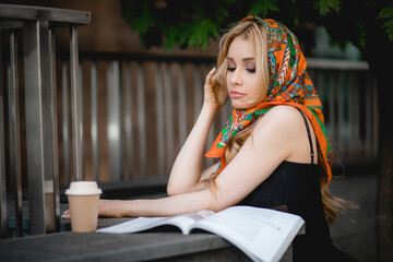 Portrait of young flawless woman titivating long blond hair, wearing black dress, silk colorful printed kerchief