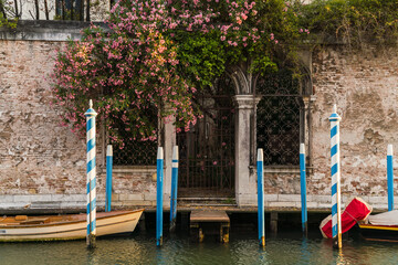 Charming facade in Venice, Italy with pink flowers hanging over and boat docked