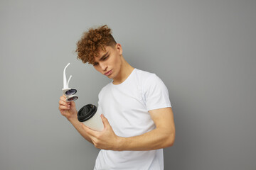 surprised by the taste of the drink, the man stands on a gray background holding a cardboard cup and looks at him holding his glasses with his hand