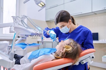 Female doctor dentist treats teeth to a child girl using anesthesia.