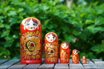 A row of nesting dolls in close-up against a background of green foliage. Slavic culture.