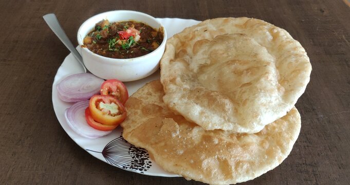 Chole Bhature or Chick pea curry and Fried Puri served in terracotta crockery over white background. selective focus
