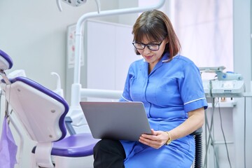 Doctor nurse dentist sitting in the office using a laptop.