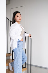 beautiful smiling young asian woman with long dark hair in white shirt on stairs at modern interior