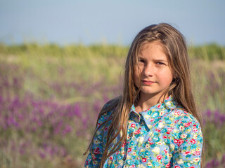 Fototapeta premium Portrait of a beautiful girl in an amazing blooming field. Nature, recreation and lifestyle. Teenage girl in a dress enjoying nature