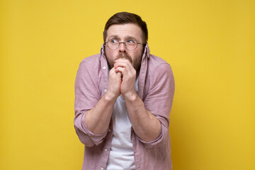 Man is anxious and frightened, he pulled his shirt over his ears and listens to every rustle, hands clasped to mouth. 