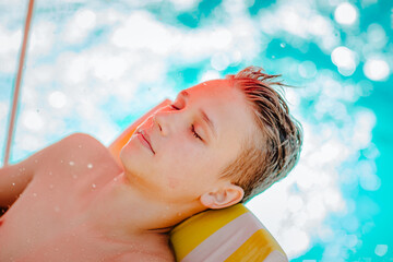 Teen boy with blond wet hair relaxing on stripped beach chair