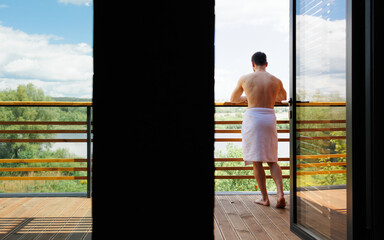 Rear view of a naked man in a towel on the balcony of his spa hotel room
