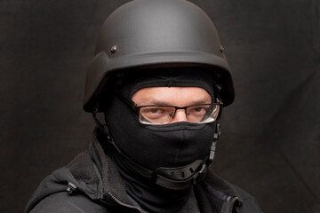 Portrait of a military man with glasses, wearing a bulletproof vest and balaclava, an army helmet on his head, black background. Concept: military journalist, volunteer at war, war in Ukraine.