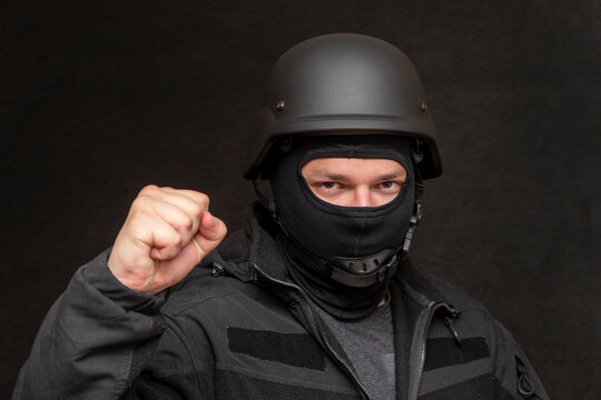 Portrait of a military soldier clutching his fist, wearing a bulletproof vest and balaclava, army helmet on his head, black background. Concept: volunteer at war, war in Ukraine, civil self-defense,