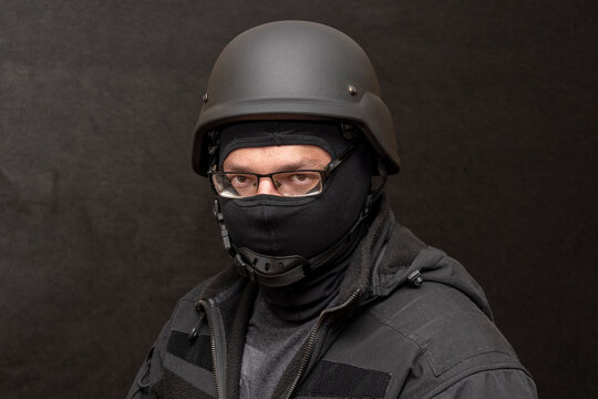 Portrait of a military man with glasses, wearing a bulletproof vest and balaclava, an army helmet on his head, black background. Concept: military journalist, volunteer at war, war in Ukraine.