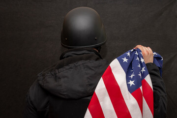 a military soldier in a helmet holds an American flag on a black background in his hand.
