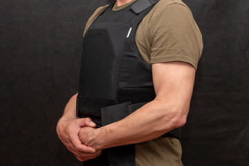 A muscular military man in a bulletproof vest on a black background. - obrazy, fototapety, plakaty