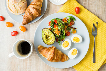 Eggs, vegetable salad with tomatoes, bacon and avocado and croissant. healthy breakfast