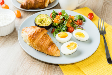 Eggs, vegetable salad with tomatoes, bacon and avocado and croissant. healthy breakfast
