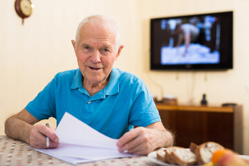 Cheerful elderly man sitting at home table with papers