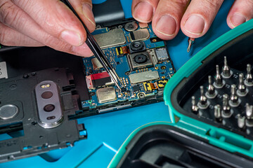 Smartphone repair in a service center. Hands of a professional master repairman repairing disassembled into pieces cell phone. Internal parts, chips, motherboards, wiring, fixing process