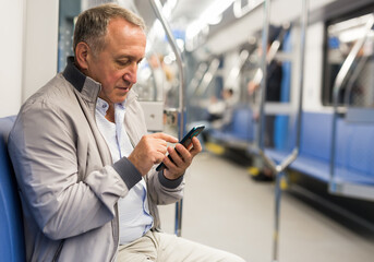 Elderly passenger is engrossed in information on smartphone while traveling in subway car