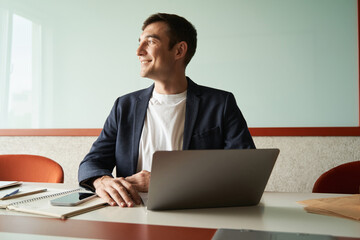 Happy office worker near laptop admiring view from window