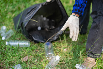 A man's hand puts plastic bottles in a black garbage bag to clean in the park. avoid pollution It is environmentally friendly and ecologically clean on Earth Day and can be sold for free income.
