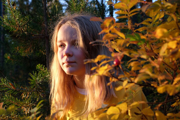 Portrait of blonde girl hiding behind a tree branch with sunlight