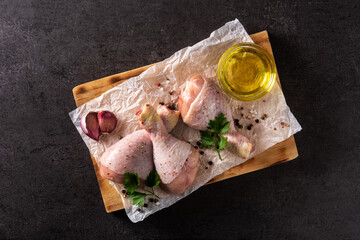 Raw chicken meat legs with spices and herbs on black background. Top view