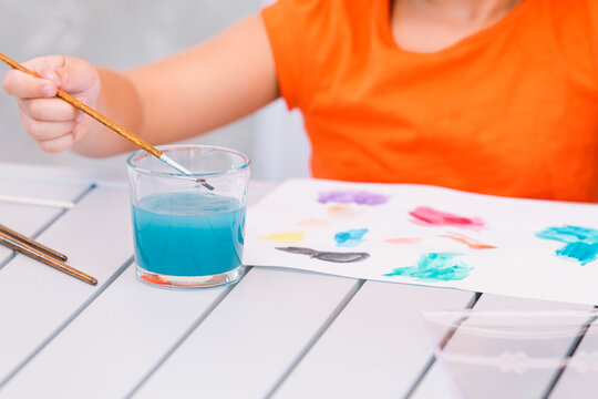 Faceless kid washing paintbrush in glass