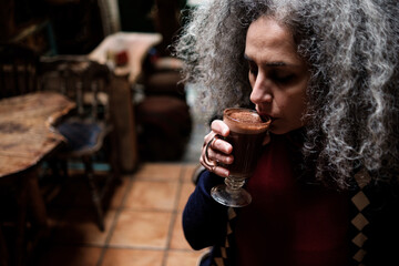 An iranian mature woman is having a mocha coffee in a cozy interior space.