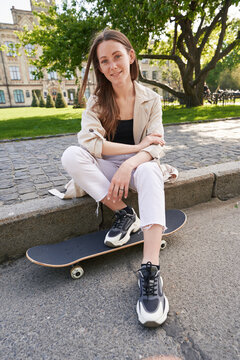 Lady sits on sidewalk in park putting feet on skateboard