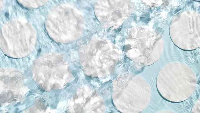 Poured water splashing and making ripples over cotton pads arranged in rows on blue background | skincare background, cleansing lotion commercial