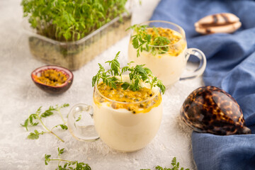 Yogurt with passionfruit and marigold microgreen in glass on gray. Side view, selective focus.