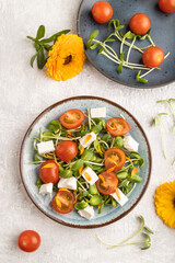 Vegetarian salad of tomatoes, marigold, microgreen, feta cheese on gray. Top view.