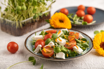 Vegetarian salad of tomatoes, marigold, microgreen, feta cheese on gray. Side view, selective focus.