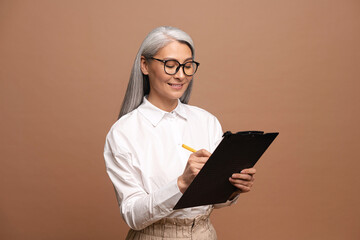 Senior confident business woman writing at the clipboard. Mature female employee in formal wear...