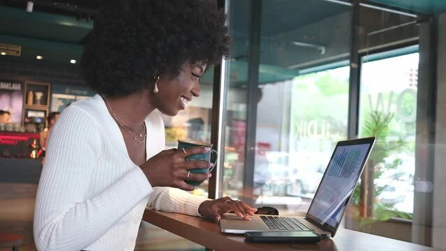 Happy African American woman sitting in cafe with coffee working on laptop and phone, freelance 