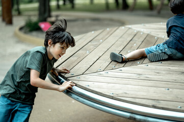 boys are walking on the playground, a boy is spinning a carousel, children are having fun on a walk...