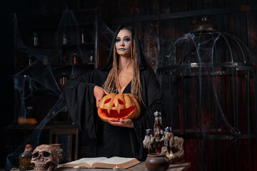Halloween concept. Black witch holding Halloween pumpkin with carved smily face in hand standing...