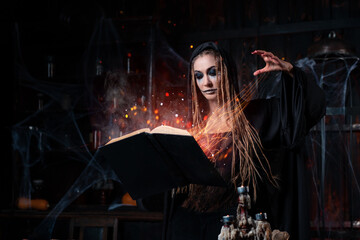 Fototapeta na wymiar Halloween concept. Witch dressed black hood with dreadlocks standing dark dungeon room use magic book for conjuring magic spell