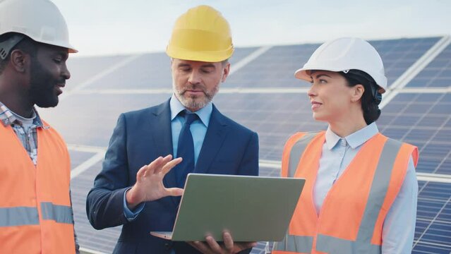 Close-up of two solar panel technicians standing outside in hard hats and listening to plan to place new batteries from company's manager.