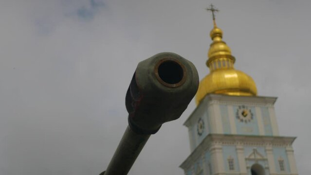 Close up of silenced tank barrel with golden church dome in background. Concept of duality between good and evil, war and peace, life and death. barrel of a tank defending beautiful Christian chapel 
