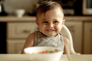 cute smiling baby eats colorful cereal flakes for breakfast. The child is happy, he is sincerely happy and smiling