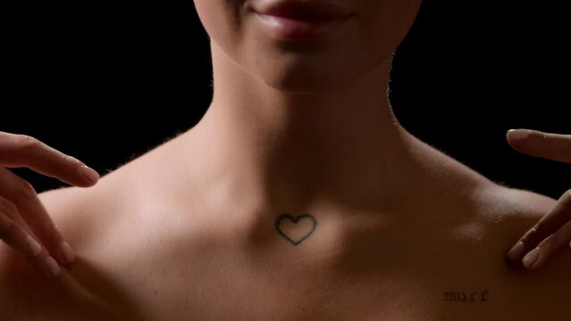 Big close-up shot of good-looking young slim white-skinned woman with bare shoulders strokes her clavicles smiling on black background | Skin hydration concept