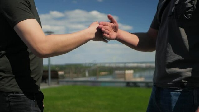 Two white guys greeting each other with cool modern handshake. Slowed down shake of hands between two young zoomers. Close up of a pair of caucasians grasping hands in trendy handshake sequence
