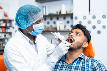 dentist with surgical gloves and face mask checking teeth of patient at hospital or clinic -...