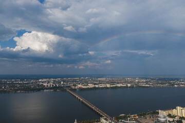 Beautiful rainbow after the rain on the blue sky and clouds over the city. An amazing natural phenomenon when sunlight is combined with rain. Photo taken from a drone