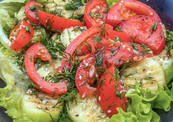 Summer salad with tomato, cucumber, lettuce, dill and sesame seeds on a dark plate. Close-up, selective focus.