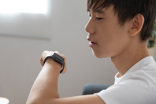 Asian teen boy talk on smartwatch in the living room at home.
