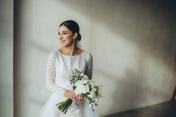 young bride in white wedding dress holding bouquet and looking away at home