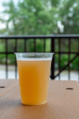 A male reaches for a tall clear glass of sour craft beer in a microbrewery. The cold refreshment has frost on the glass. The beer is on a table and coaster. The top of the glass has white froth. 